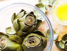 artichokes in a glass bowl with oil and leaves on the table next to them