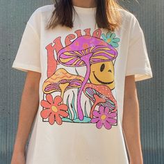 This Groovy Tee Is A Must Have, "Hello" Written In Retro Font With A Super Cool Graphic Which Includes Mushrooms, Flowers And A Sinking Smiley Face. Has Some Distressing & Little Holes To Give It That Worn In Vintage Look. Oversized Style Which Pairs Perfect With Biker Shorts! 95% Cotton & 5% Spandex Model Is Size Small Wearing Size Small Measurements: S: Chest 42" & Length 28" M: Chest 45" & Length 28.5" L: Chest 58" & Length 29" Brand New! From My Boutique! Casual Mushroom Print T-shirt For Spring, White Mushroom Print Top For Summer, Spring Cotton Tops With Mushroom Print, Spring White Tops With Mushroom Print, White Mushroom Print Top For Spring, Spring White Top With Mushroom Print, Spring Cotton Top With Mushroom Print, Spring Mushroom Print Relaxed Fit Top, Spring Mushroom Print Graphic Tee