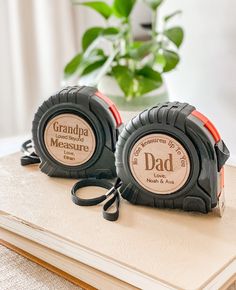 two personalized tape measures sitting on top of a wooden table next to a potted plant