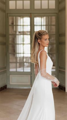 a woman in a white wedding dress is walking through an open room with large windows