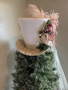 a white hat with feathers and flowers on top of a green christmas tree in front of a wall