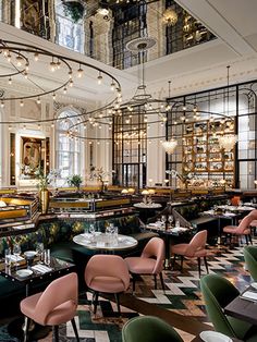 the interior of a fancy restaurant with green and pink chairs, tables, and chandeliers