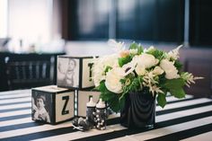 a vase with flowers on top of a black and white striped table cloth next to two cubes