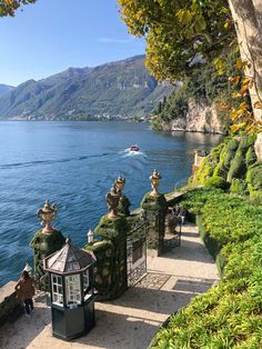 some people are standing on the edge of a walkway next to water and mountains in the background