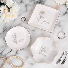 wedding rings, bracelets and jewelry laid out on a marble counter top with flowers