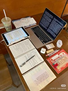 an open laptop computer sitting on top of a wooden table next to papers and pens