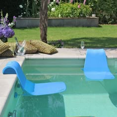 two lawn chairs sitting in the middle of a swimming pool next to flowers and plants