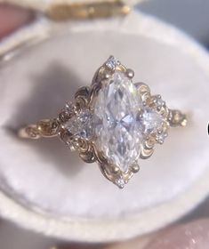 a close up of a person holding a ring in their hand with an oval shaped diamond surrounded by smaller round diamonds