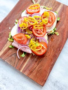 a wooden cutting board topped with sliced tomatoes and onion on top of lettuce