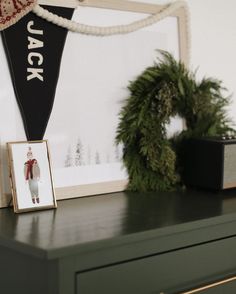 a green dresser with a black and white flag hanging on it's side next to a christmas wreath