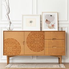 a wooden cabinet with two pictures on top of it next to a rug and vase