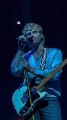 a young man holding a guitar and singing into a microphone on stage at a concert