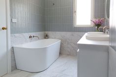 a large white bath tub sitting next to a sink in a bathroom under a window