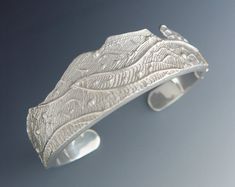 a silver cuff with leaves on it is sitting on a gray surface and looks like something out of the woods