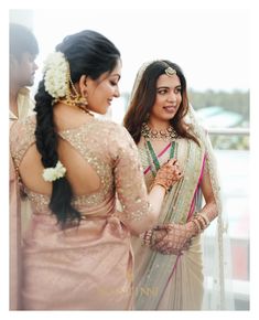 two women standing next to each other in front of a window and one is wearing a pink sari