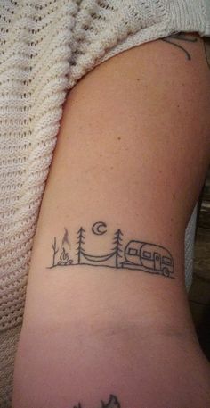 a woman with a tattoo on her arm has a camper and trees in the background