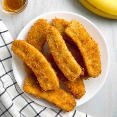 fried fish sticks on a white plate next to a banana