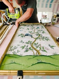 a man is working on an art project with green and white fabric, which has a tree painted on it