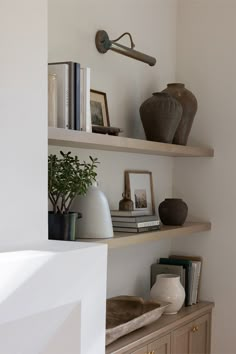 White oak open shelves staged and styled with various decorative pieces. Above the shelves is a antique brass picture light. Beside the shelves is a custom fireplace surround finished with Roman Clay. Built Ins With Picture Frames, Open Door Living Room, Floating Shelves With Lights Living Room, Shelf With Candles, Light Over Built Ins, Picture Frame On Shelves, Lights Above Floating Shelves Living Room, Light Above Shelves, Picture Light Over Shelves