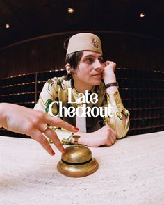 a woman sitting at a table with a bell in front of her and the words late checkout written on it