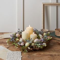 some candles are sitting on a table with flowers and eggs in the center, next to an empty photo frame