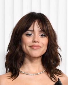 a close up of a person wearing a black dress and smiling at the camera with white curtains in the background