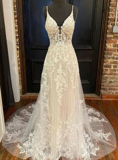 a white wedding dress on display in front of a door with a brick wall behind it