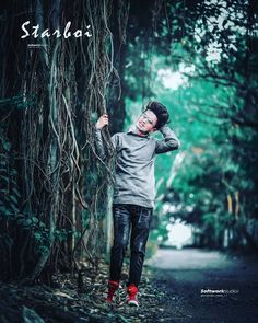 a young boy standing in front of a tree with vines on it's branches