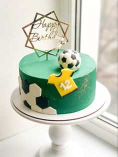 a birthday cake decorated with soccer balls and a star on top, sitting in front of a window