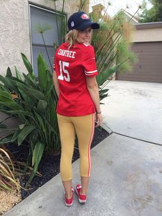 a woman standing on the sidewalk in front of a house wearing a football jersey and matching leggings