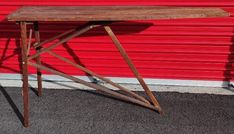 an old wooden table sitting in front of a red garage door on the side of a building