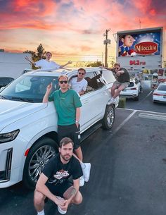 some people are posing in front of a white car with an advertisement on the back