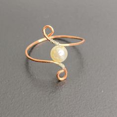 a wire wrapped ring with a yellow glass bead on it's end, sitting on a gray surface