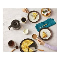 two people eating breakfast at a table with cups and saucers on it, one person holding a fork