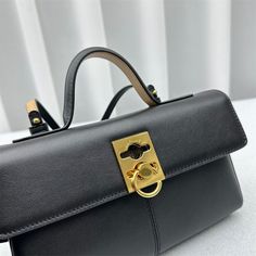 a black handbag with a gold lock on the front and side handles, sitting on a white surface