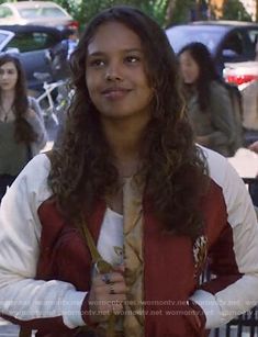 a woman with long hair wearing a red and white jacket standing in front of a fence