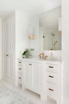 a bathroom with white cabinets and marble counter tops, gold faucets and mirrors