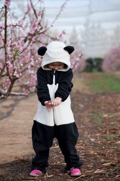 a small child wearing a panda costume standing in front of a tree with pink flowers