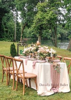 a table set up with flowers and greenery for a formal dinner in the park