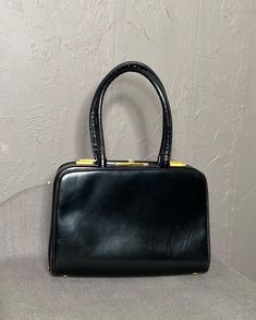 Vintage 1950's Leather Handbag from KORET. Smooth, Structured Black Leather with Sateen Black + Copper Brown fabric lining and Gold tone hardware. Beautifully made bag with amazing details, it's easy to see why KORET is so coveted! Small Doctor style satchel with two handles. Gold push lock. Accordion style with structured frame and leather panels at sides. 4 Gold tone "feet" on base. Delicate gold chain attached to Sateen kiss-lock coin purse. One Zippered pocket and 2 open pockets on interior. Copper Brown Sateen lines the pockets on interior, such an elegant touch. Light signs of wear all over with slight cracking on handles. Lining is CLEAN. Overall condition 8/10. Please inspect+ zoom photos to see condition. Measurements taken from outside of bag. Width : 9.5" Height : 6.5" Depth : 3 Vintage Black Top Handle Satchel, Black Handheld Satchel With Gold-tone Hardware, Doctor Style, Retro Black Bags With Gold-tone Hardware, Black Leather-handled Satchel Box Bag, Luxury Black Satchel With Turn-lock Closure, Delicate Gold Chain, Black Leather Handbag, Copper Brown