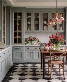 a kitchen with checkered flooring and cabinets in grey tones, pink flowers on the table