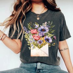 Introducing the Boho Wildflowers Shirt - a delightful and thoughtful gift for her that beautifully captures the essence of nature and free-spirited style. Crafted from the finest, softest cotton, this floral tee is a wearable celebration of the blooming wildflowers that inspire joy and tranquility. Its charming design, featuring an array of intricately illustrated wildflowers, makes it a perfect shirt for flower lovers and a trendy addition to any wardrobe. PRODUCT DESCRIPTION: Made with 100% Ai Multicolor Tops For Spring As A Gift, Cotton Tops With Plant Print, Cotton Tops With Plant Print As Gift, Cotton Tops With Plants Print For Gift, Cotton Tops With Plant Print For Gifts, Mother's Day Floral Print Short Sleeve Top, Floral Print Summer Tops As A Gift, Floral Print Short Sleeve Top As Gift, Floral Print Short Sleeve Top