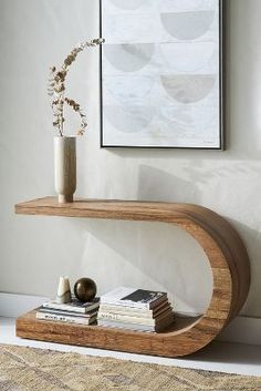 a wooden shelf sitting on top of a white wall next to a vase and books