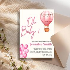 a pink hot air balloon baby shower is on the table next to a white envelope