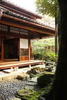 a japanese style house with rocks and trees in the foreground, near a stream