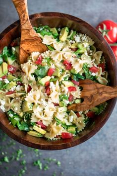 a wooden spoon in a bowl filled with pasta and veggies next to tomatoes