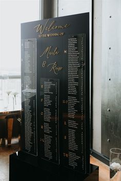 a black menu board with gold lettering on it and wine glasses next to it in front of a window