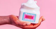 a hand holding a jar of whipped cream on a pink background with the words free hugs written in it