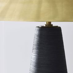 a black lamp with a gold shade on it's side and a white wall in the background