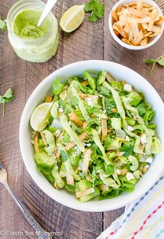 a white bowl filled with lettuce salad next to two small bowls of chips